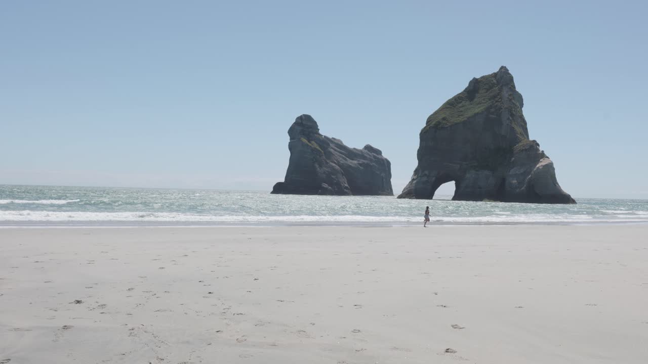 joven mujer caucásica corriendo en la playa de wharariki en un día soleado en nueva zelanda