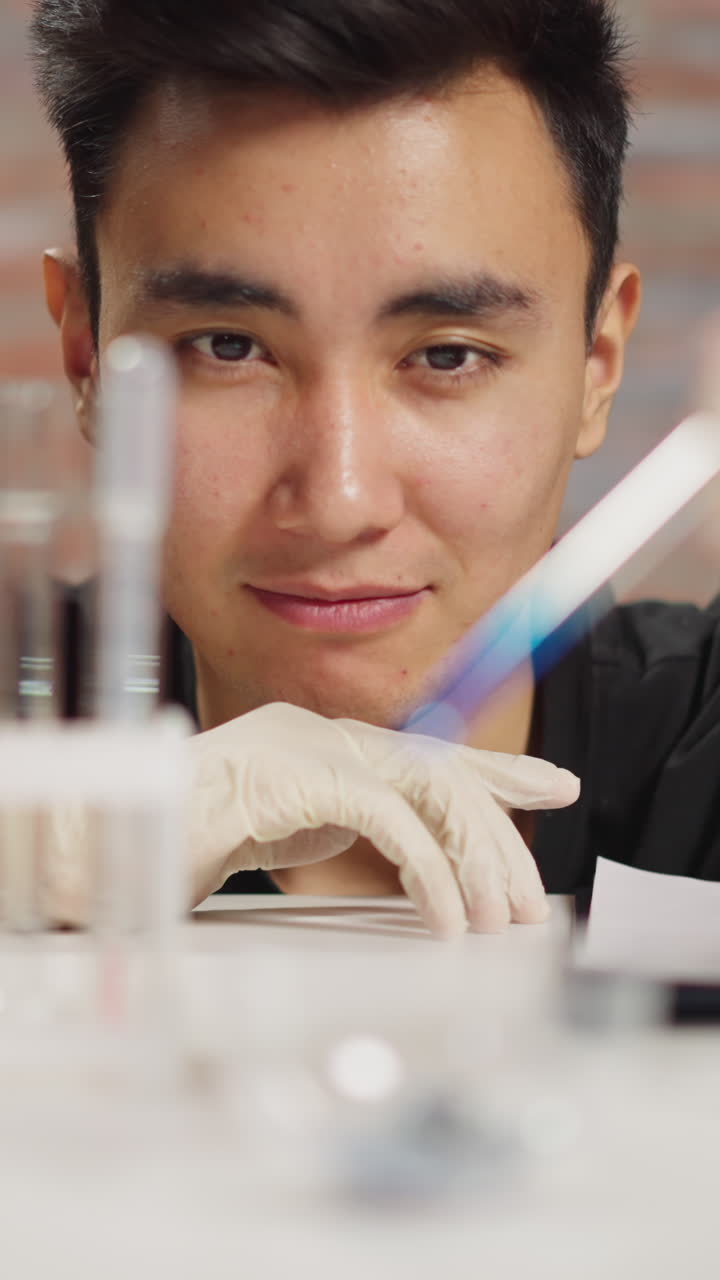 Happy lab assistant works with materials and reagents leaning on table with different lad glassware in scientific laboratory close view