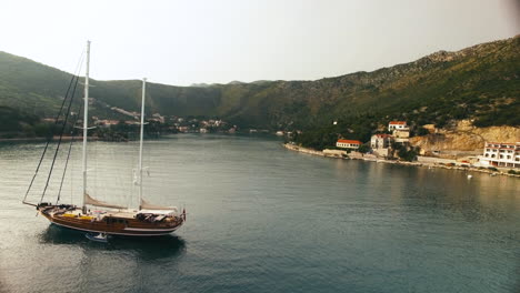 Aerial-shot-of-a-sailboat-in-Croatia,-while-moving-in-a-little-lake-with-a-town-in-the-background