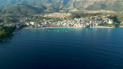 Pequeña-Ciudad-Costera-En-El-Sur-De-Albania-Con-Una-Pequeña-Playa-Y-Montañas-Al-Fondo