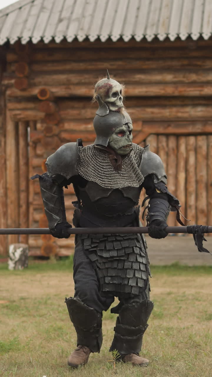 caballero espeluznante con cráneo en el casco corre sosteniendo la lanza amenazadoramente lluvia. guerrero malvado se apresura a la batalla moviéndose fuertemente en el asentamiento medieval con edificios de madera