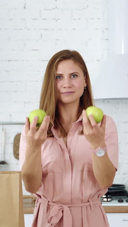 a girl in a white kitchen near a grocery bag holds green apples in her hands. vertical video
