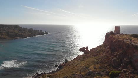 AERIAL:-Beautiful-Ghajn-Tuffieha-Bay-against-the-sun-with-Tower-in-Malta