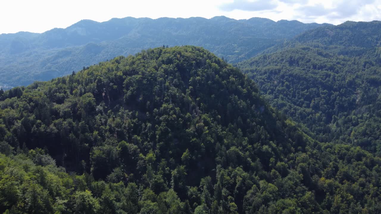 vuelo aéreo hacia un enorme monte boscoso en un paisaje alpino verde
