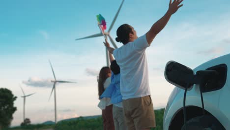 Concepto-De-Familia-Feliz-Progresiva-En-El-Parque-Eólico-Con-Vehículo-Eléctrico.