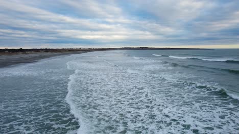 aerial of ocean waves crashing on a beach on a cloudy day