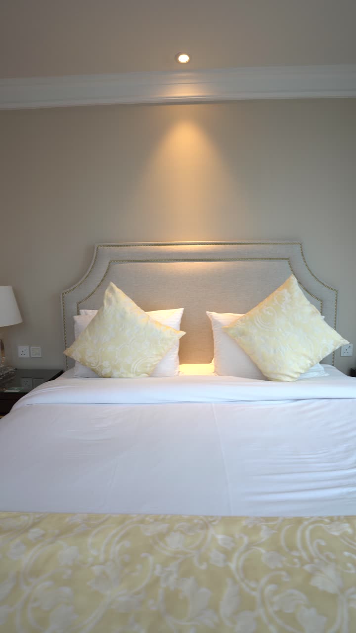 Tampilan jarak dekat tempat tidur hotel yang besar dan nyaman dengan seprai putih bersih, bantal kuning yang elegan, dan bed runner bermotif