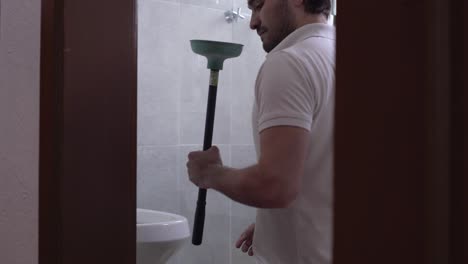 young muscular man unclogging a toilet