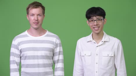 two young multi-ethnic businessmen smiling together against green background