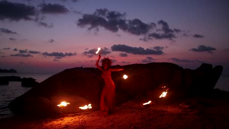 slow motion of erotic and sensual belly dancer performing figure 8 move with fire palm torch props, on the beach during golden hour