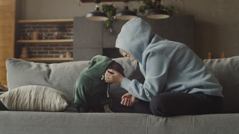 red haired woman caresses her bulldog dog dressed in a sweatshirt while sitting on the couch in the living room at home