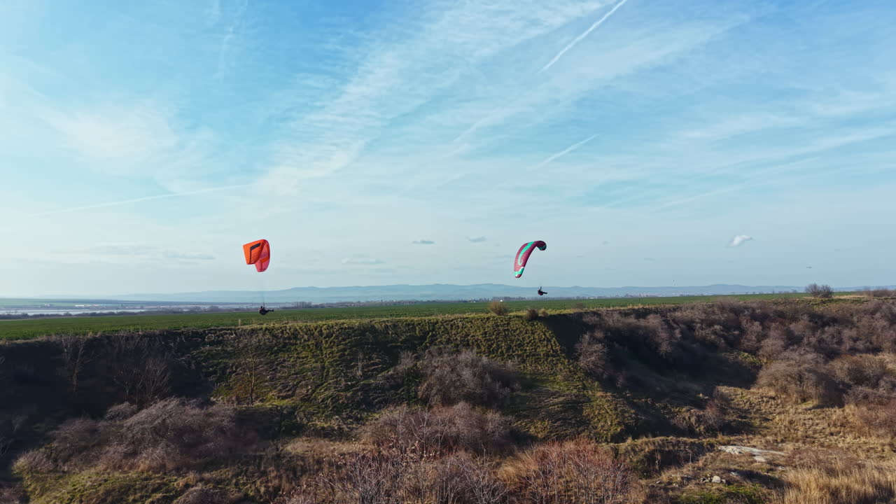Persone che fanno volare aquiloni sopra un campo verde vicino a una scogliera in una giornata di sole con un cielo sereno sullo sfondo e nuvole sparse sopra