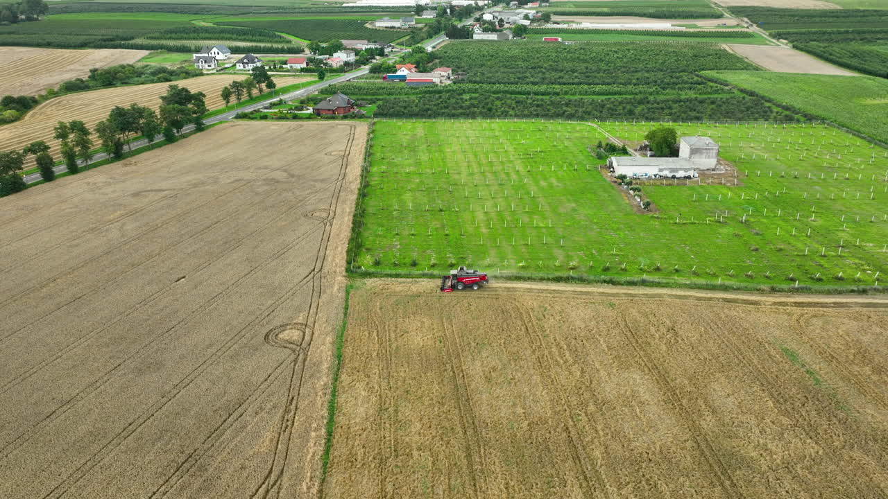 먼 곳 에 농장 이 있는 초록색 과수원  에 있는  에서 일 하는 빨간색 수확기 의 공중 사진