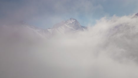 Video-Einer-Drohne,-Die-Durch-Die-Wolken-Auf-Eine-Schneebedeckte-Bergkette-Zufliegt