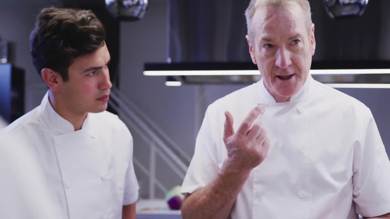 cocinero profesional caucásico en una cocina de un restaurante degustando comida con un cocinero aprendiz