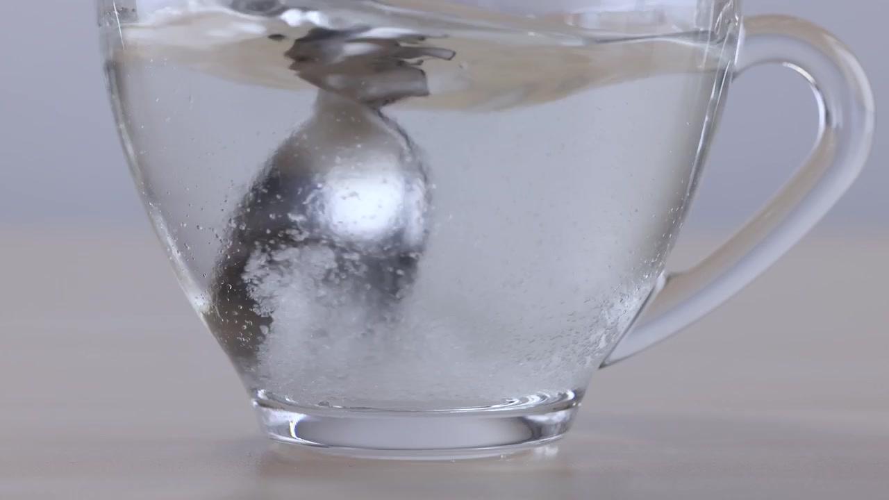 Cucchiaio di metallo che mescola una compressa effervescente in un bicchiere di vetro.