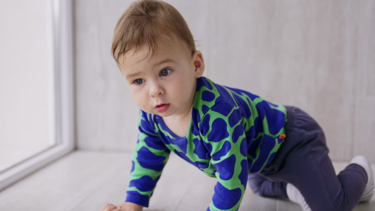 Sweet toddler boy crawling on the floor by the panoramic window. Close up. Ball at the backdrop in blur.
