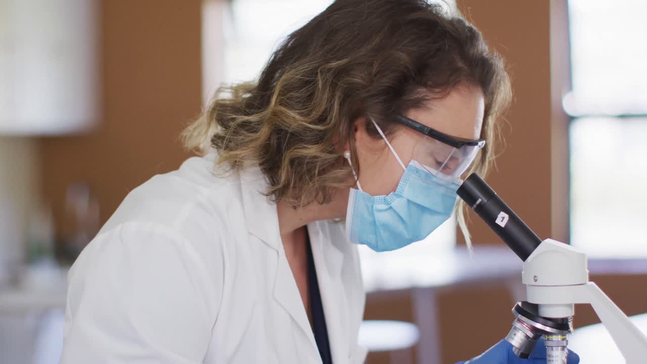Insegnante donna che indossa maschera facciale e occhiali protettivi utilizzando il microscopio in laboratorio