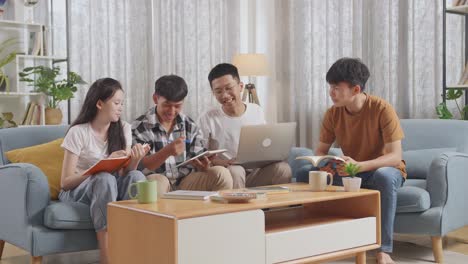 asian teen group studying at home. a boy holding a laptop discussing with his friends, writing into notebook. a boy in plaid shirt with a book teaching a girl and frends.