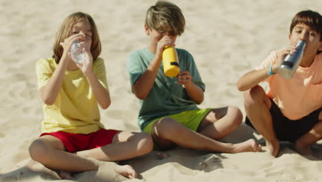 boys sitting on beach and drinking water after playing football