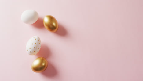 close up of white and gold easter eggs on pink background with copy space