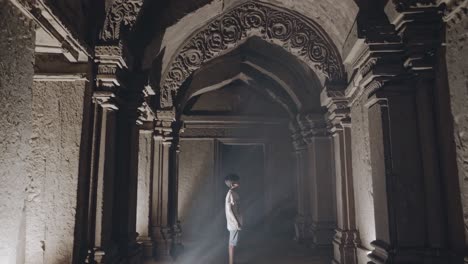 sunbeam illuminating a young boy standing in a mystical hallway adorned with ornate columns and decorated arches, revealing the wonders of an ancient temple in asia