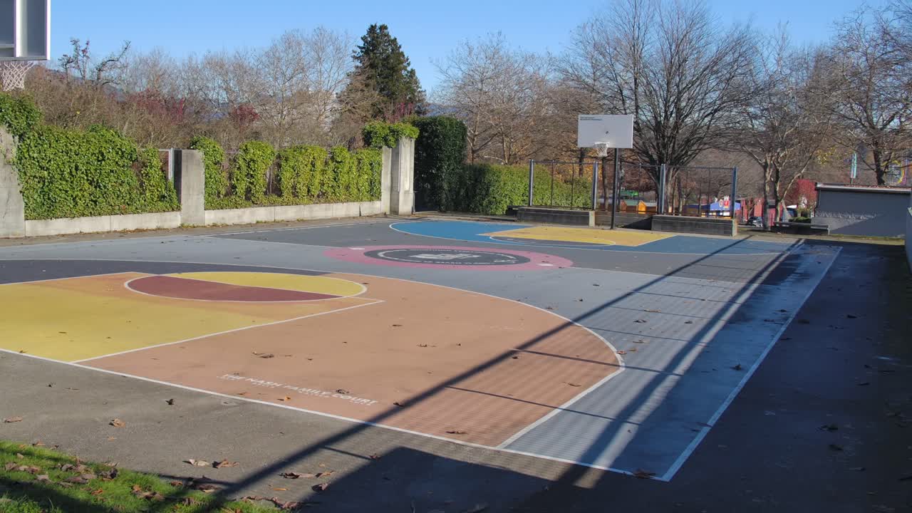 Empty basketball court in Vancouver on a sunny day, clear shadows cast by leafless trees, urban setting