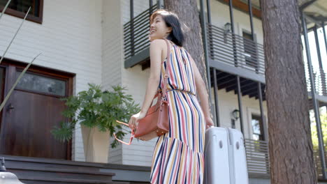 happy asian woman with suitcase walking on stairs of home on sunny day, slow motion