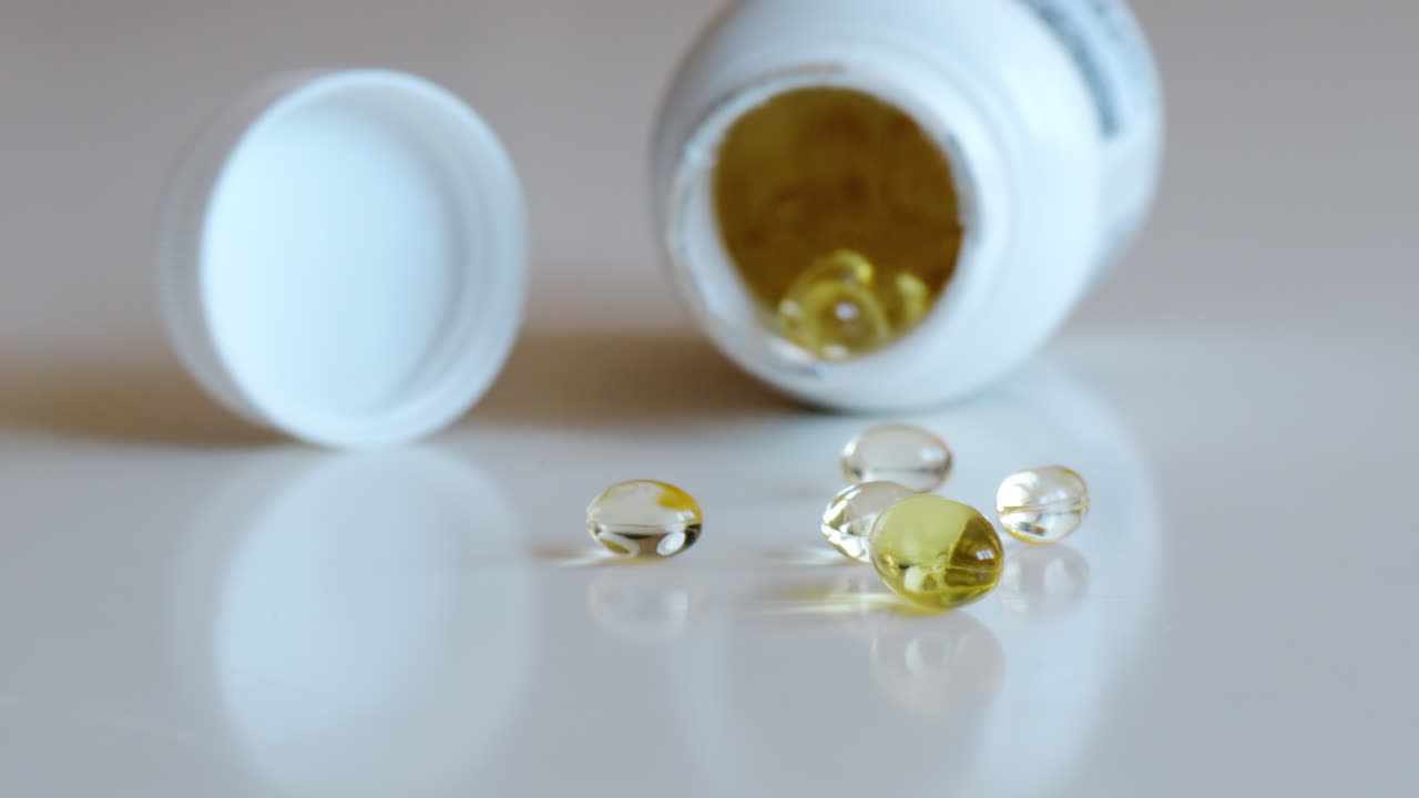 Fish oil omega 3 supplements spilling out of a packer bottle on a white background