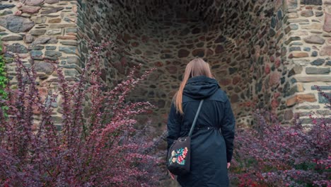 girl with long hair walks between red bushes to a stone wall in slow motion