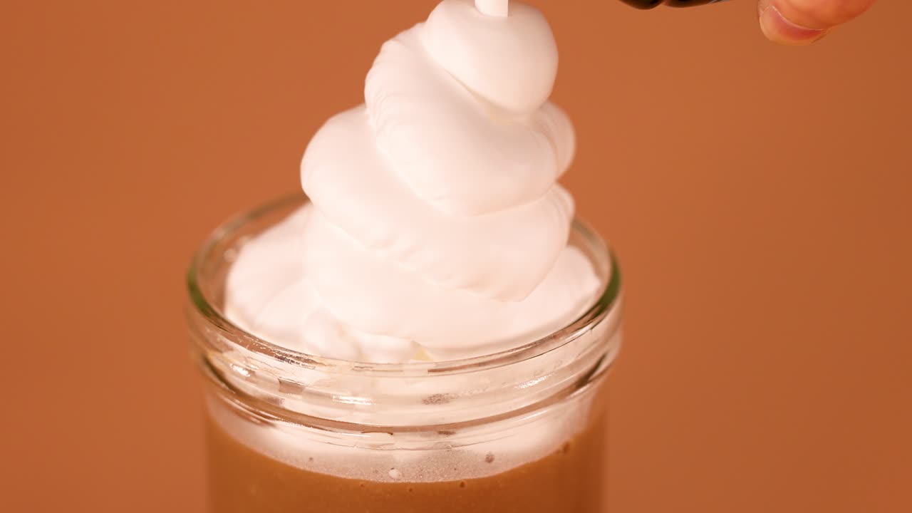 Crème fouettée onctueuse versée sur un milkshake au chocolat crémeux, gros plan, éclairage chaleureux, caméra stable