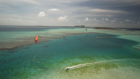 Un-Kitesurfista-Deslizándose-Sobre-Aguas-Cristalinas-De-Color-Turquesa-Cerca-De-Un-Cayo-Tropical,-Vista-Aérea