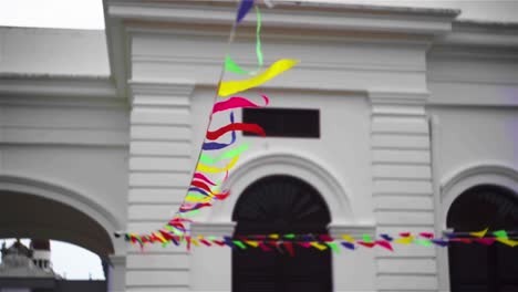 Colorful-flags-garland-outside-white-building-on-windy-day-in-Asia