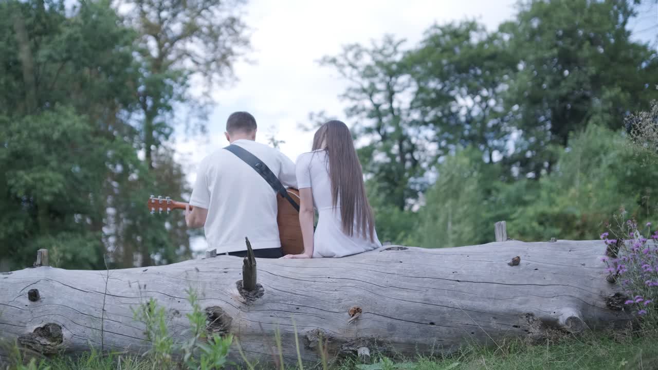 Couple sitting on a log playing guitar