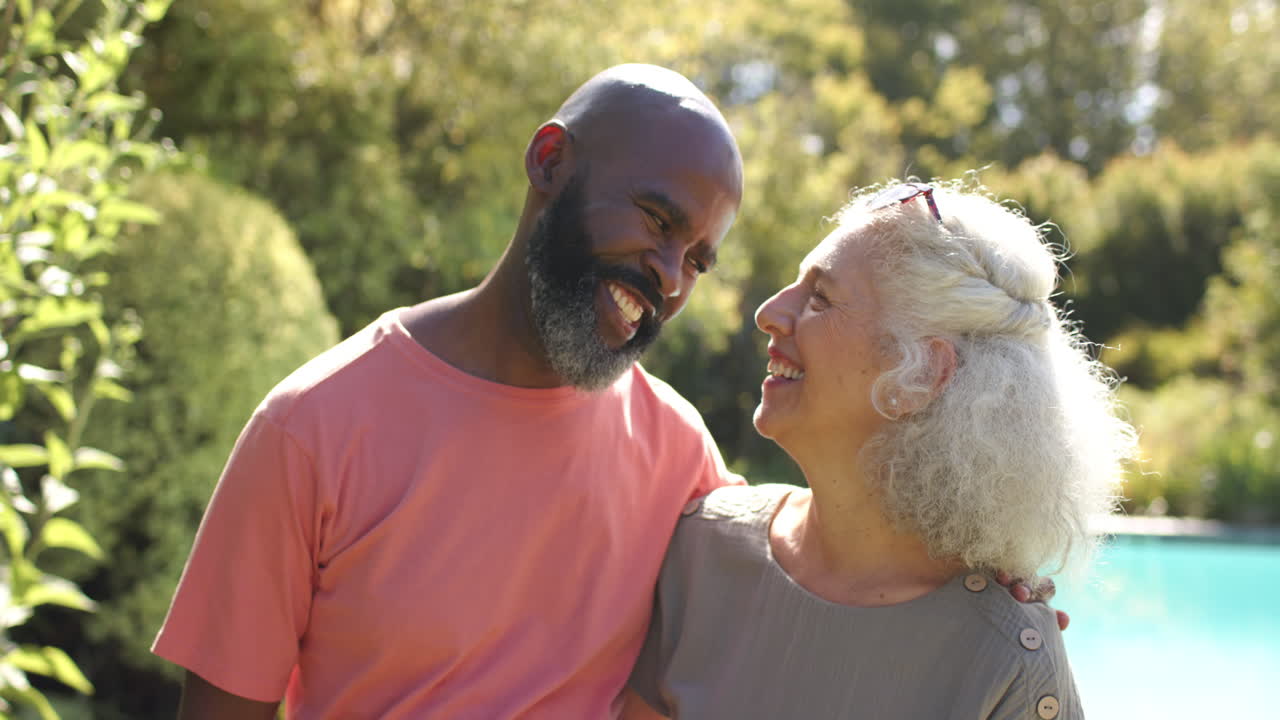 Amici anziani che si godono il tempo all'aperto insieme, sorridendo e abbracciandosi in giardino.