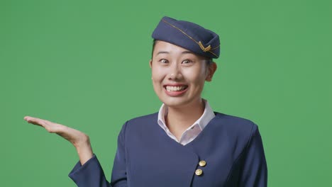 close up of asian woman air hostess smiling and pointing to side while standing in the green screen background studio