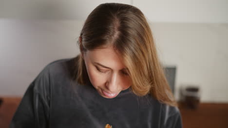 close up of young lady with long flowing hair eating meat using chopsticks in bright modern kitchen, looking down attentively at bowl, soft natural lighting with slightly blurred background