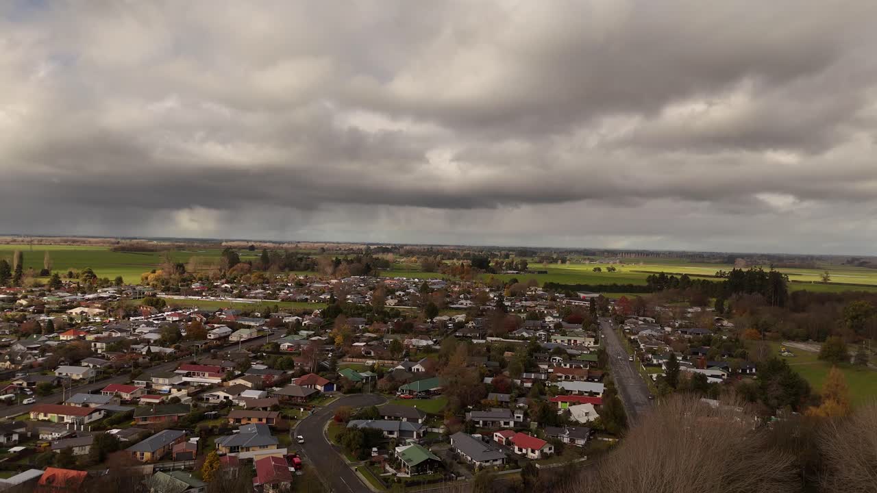 Geraldine town, residential neighborhood and surrounding green farmland under dramatic cloudy sky, South Island, New Zealand. Aerial drone