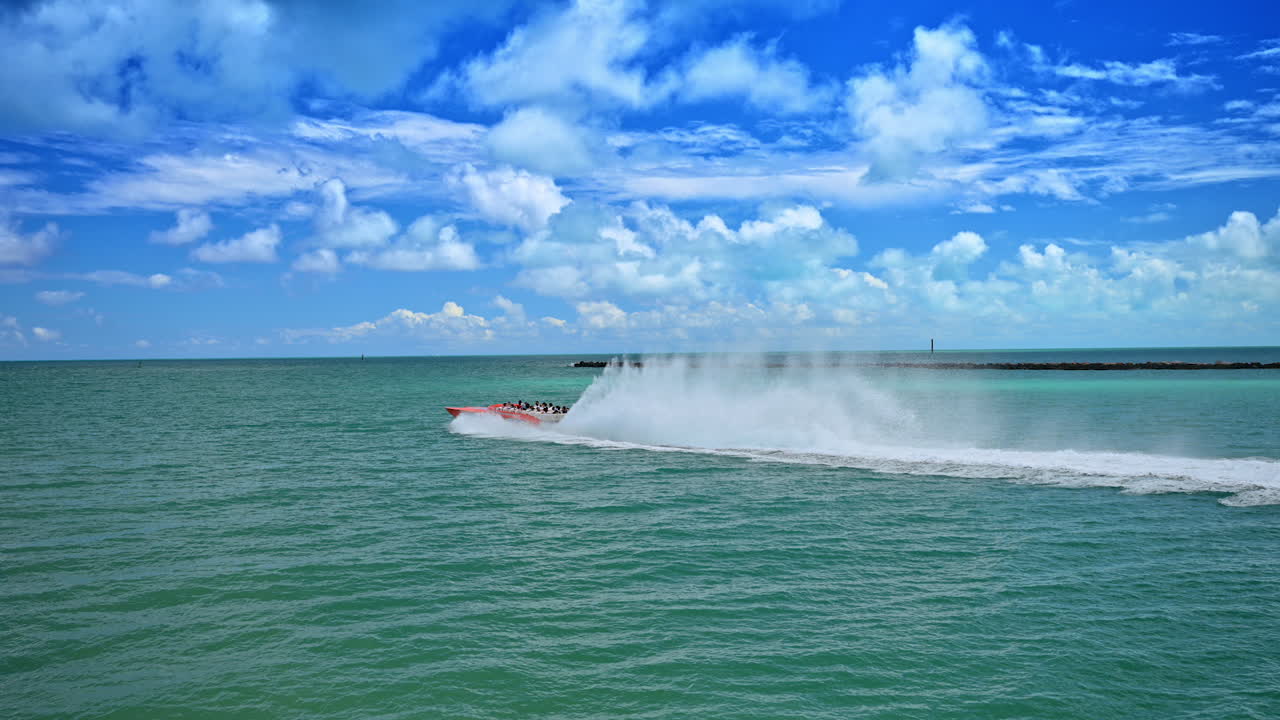 Motoscafo rosso veloce che si muove attraverso acqua turchese a Miami. Motoscafo che crea una scia bianca sulla superficie dell'oceano sotto un cielo azzurro nuvoloso.