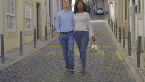 una feliz pareja multirracial caminando por la calle y mirando a su alrededor.