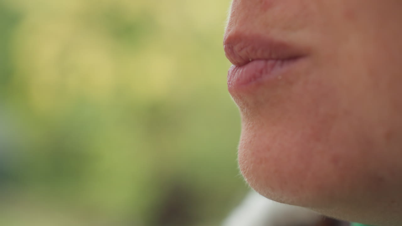Primo piano di una donna caucasica, profilo della bocca che riflette il retrogusto, leggera smorfia e masticazione, attenzione sensoriale su labbra e mento, sfondo da giardino con bokeh delicato, atmosfera calma e contemplativa e ritmo di vita lento