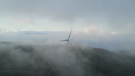 Wind-turbines-on-mountains,-generate-green-energy,-surrounded-by-clouds-in-the-sky