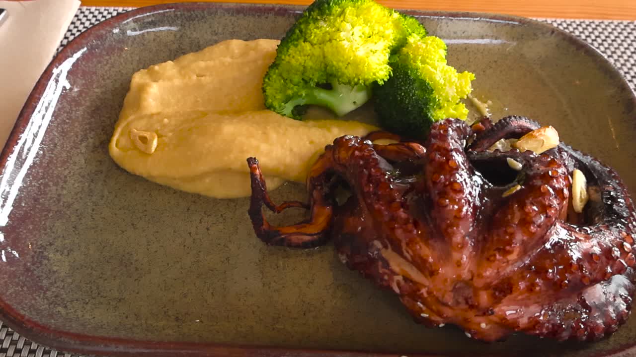 Close-up of a freshly grilled octopus dish served at a traditional Portuguese restaurant. Tender charred octopus on a plate with side vegetables, showing rich texture and fine-dining presentation