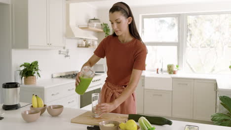 pouring green smoothie into glass, woman in kitchen embracing healthy lifestyle