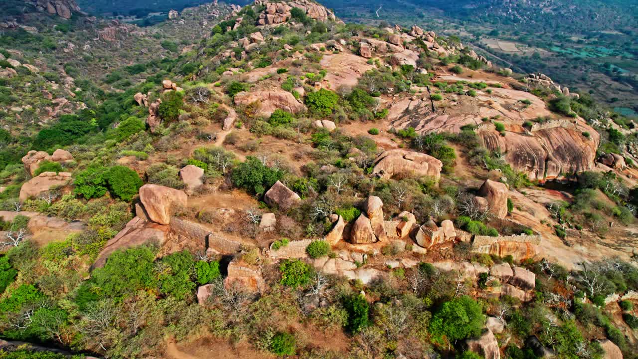 Bird eye view of big rocky hillscape with surrounded by lush greenery. day time, push in, tilt down, drone shot, 4k.