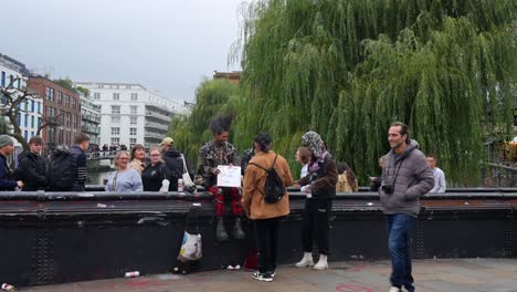 tourists in camden town observe punks seated on a bridge over the canal asking for money