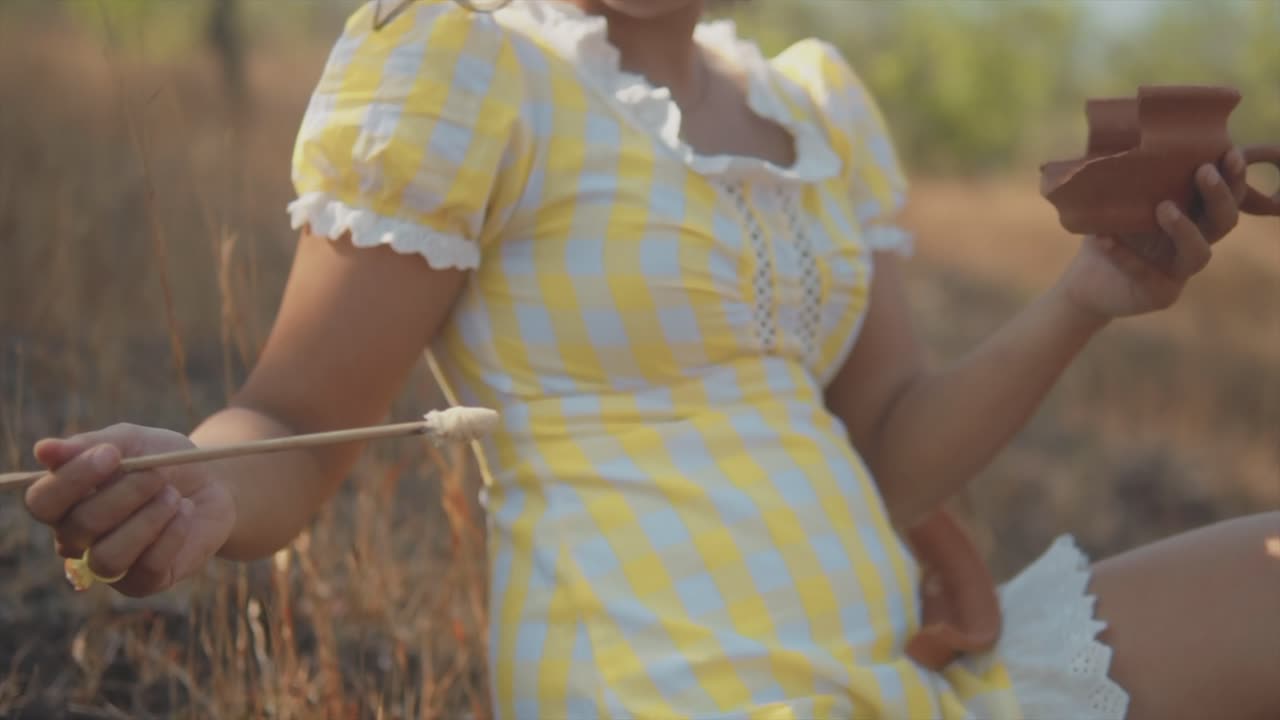 joven hermosa mujer india sumerge un cepillo en una olla que descansa en el suelo mientras arregla una olla de arcilla rota