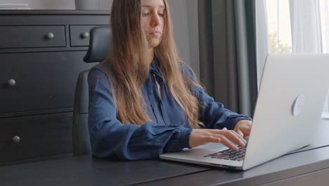 Young-caucasian-woman,-long-hair-is-typing-on-a-laptop-in-office,-working-on-a-project