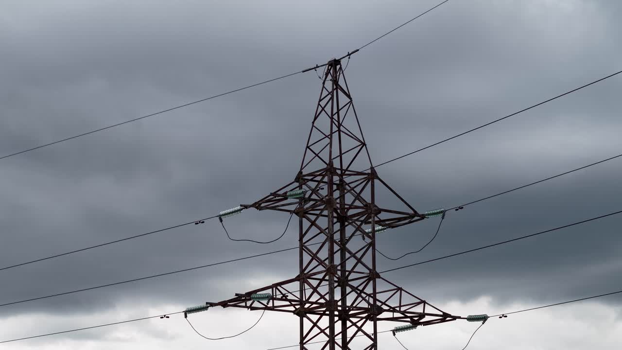 Close-up of a steel transmission tower with overhead cables under dark storm clouds, dramatic energy infrastructure silhouette against an overcast sky