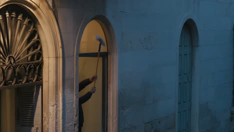 persona limpiando la ventana de un edificio histórico en venecia al anochecer, enmarcada por ventanas arqueadas